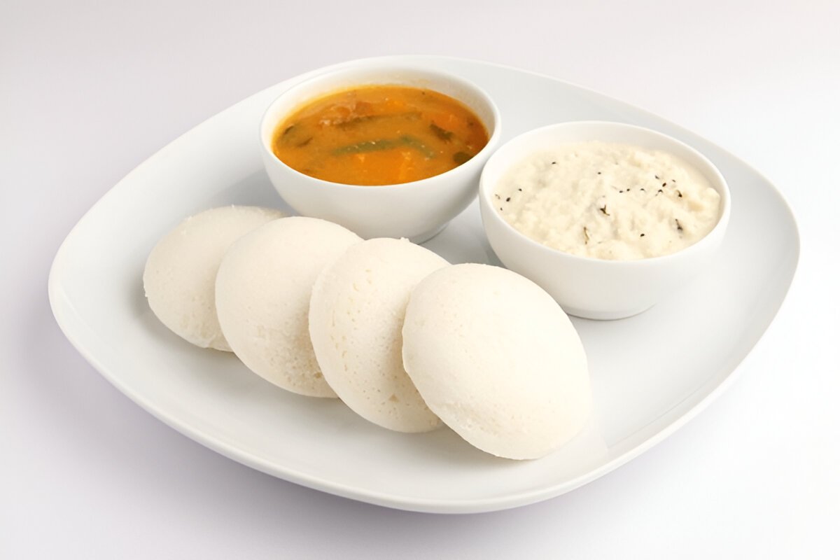 A plate of white Idlis with bowls of Sambar and coconut chutney.