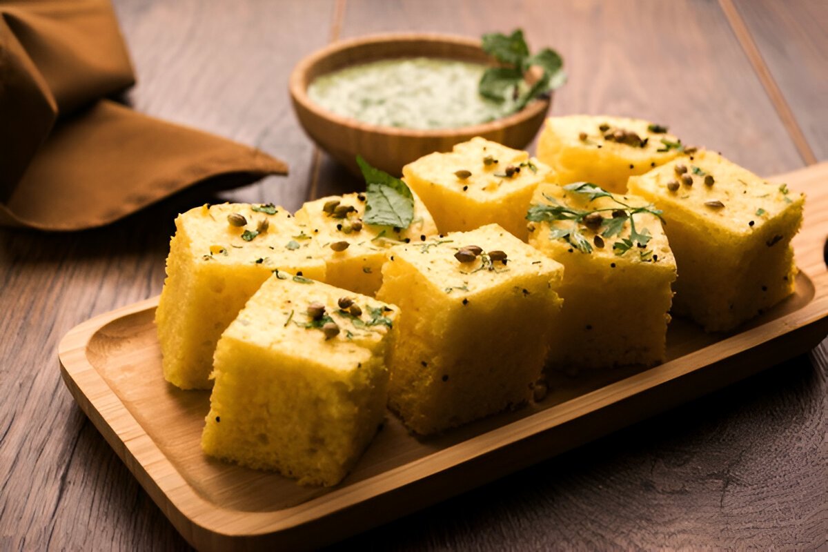 Freshly cut pieces of yellow Dhokla on a wooden tray with green chutney.